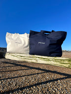 Image of both navy and natural tote bags at the beach